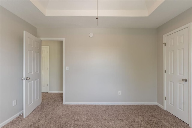unfurnished room featuring a tray ceiling, light carpet, and baseboards