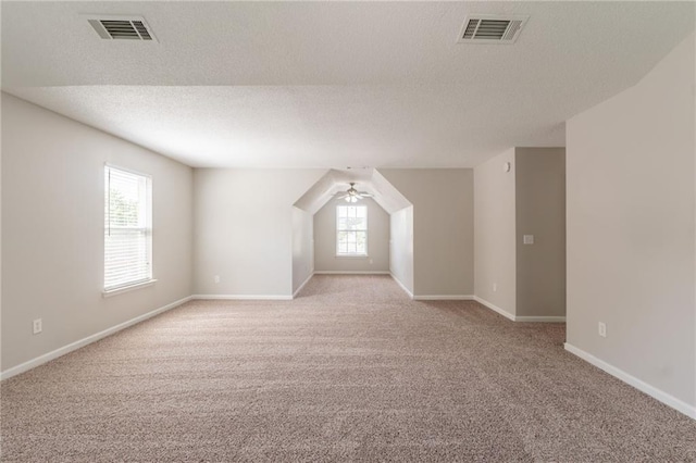 additional living space with light carpet, a textured ceiling, a ceiling fan, and baseboards