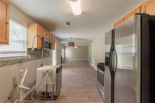 kitchen with appliances with stainless steel finishes, light wood-style floors, tasteful backsplash, ceiling fan, and a textured ceiling