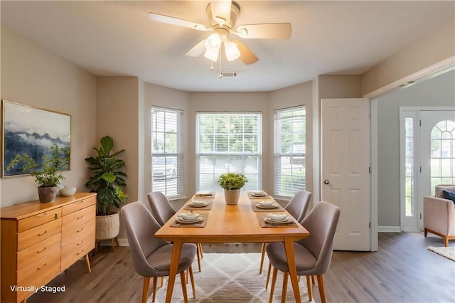 dining room with light wood-type flooring, healthy amount of natural light, ceiling fan, and baseboards