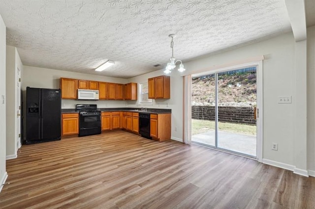 kitchen featuring black appliances, a notable chandelier, pendant lighting, and light hardwood / wood-style flooring