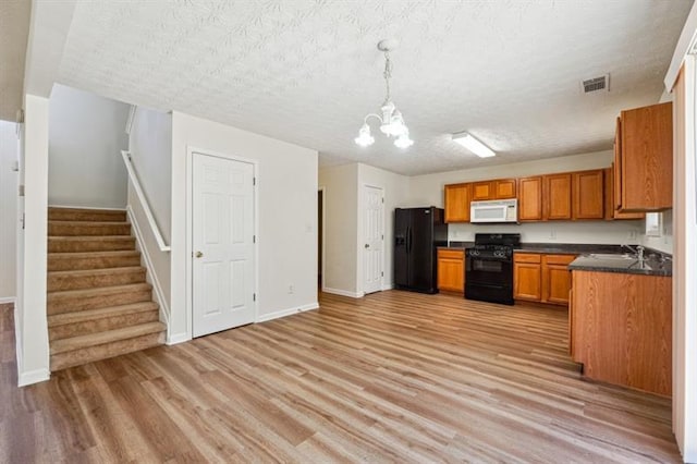 kitchen featuring an inviting chandelier, black appliances, a textured ceiling, and light wood-type flooring