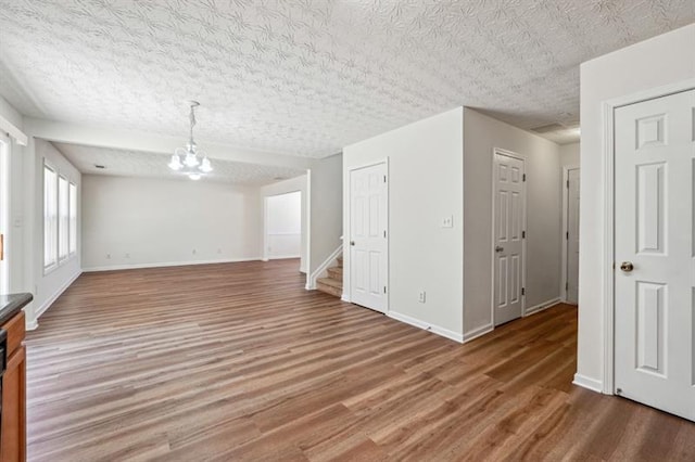 empty room with a chandelier, wood-type flooring, and a textured ceiling