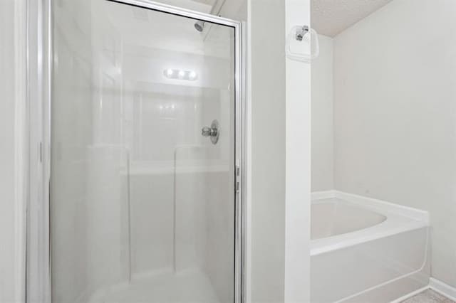 bathroom with a textured ceiling and shower with separate bathtub