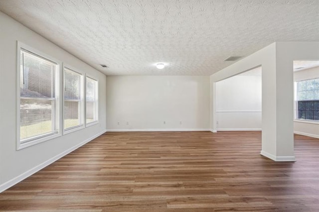 empty room with dark hardwood / wood-style flooring, a healthy amount of sunlight, and a textured ceiling