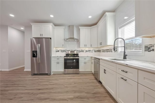 kitchen featuring sink, stainless steel appliances, light hardwood / wood-style flooring, and wall chimney range hood