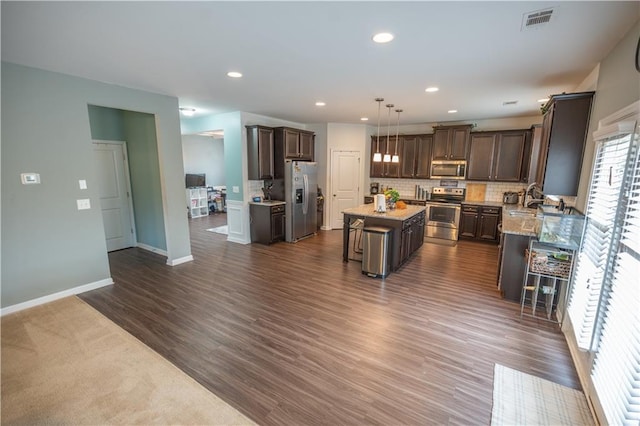 kitchen with decorative light fixtures, a center island, a kitchen breakfast bar, decorative backsplash, and appliances with stainless steel finishes