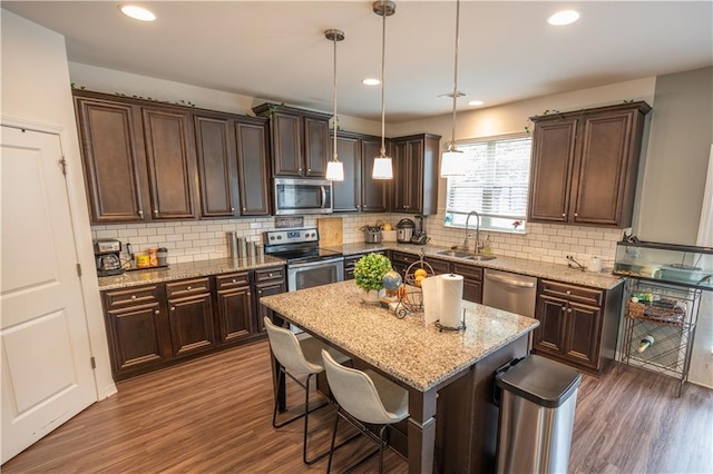 kitchen with appliances with stainless steel finishes, a breakfast bar, a kitchen island, sink, and decorative light fixtures