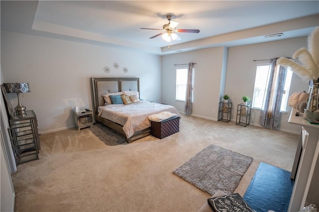 carpeted bedroom featuring a raised ceiling, ceiling fan, and multiple windows