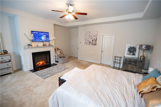 bedroom with a raised ceiling, light carpet, and ceiling fan