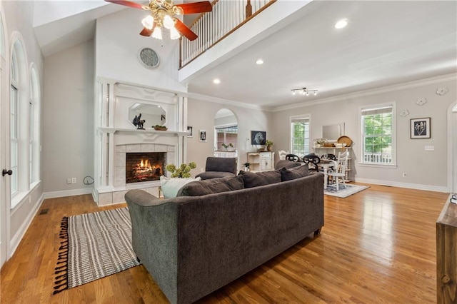 living room with ornamental molding, a tiled fireplace, light hardwood / wood-style flooring, and a high ceiling