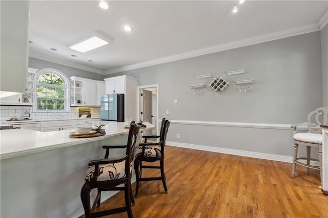 kitchen featuring crown molding, a breakfast bar area, fridge, tasteful backsplash, and white cabinets