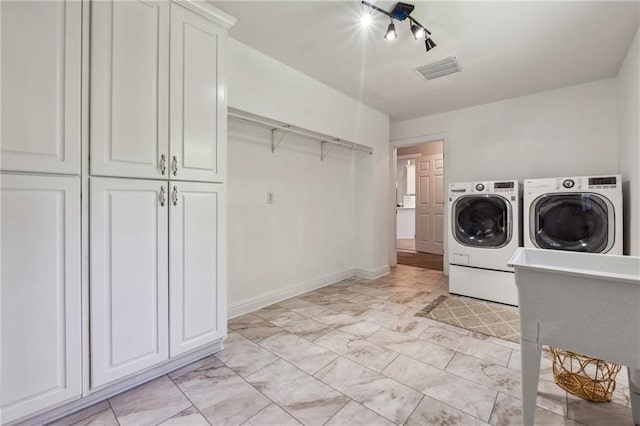 clothes washing area with cabinets, rail lighting, and washer and dryer