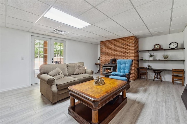 living room with french doors, a drop ceiling, a wood stove, and light wood-type flooring