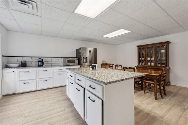 kitchen featuring a kitchen island, white cabinetry, stainless steel appliances, light stone countertops, and light hardwood / wood-style flooring