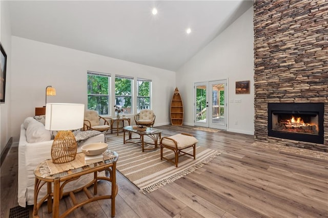 living room with high vaulted ceiling, a fireplace, light hardwood / wood-style floors, and french doors