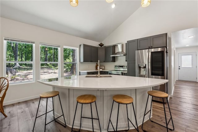 kitchen featuring a kitchen bar, sink, gray cabinetry, stainless steel appliances, and wall chimney range hood