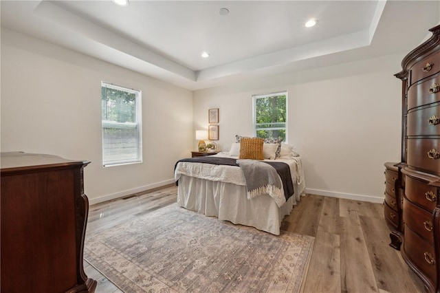 bedroom featuring multiple windows, light hardwood / wood-style flooring, and a tray ceiling