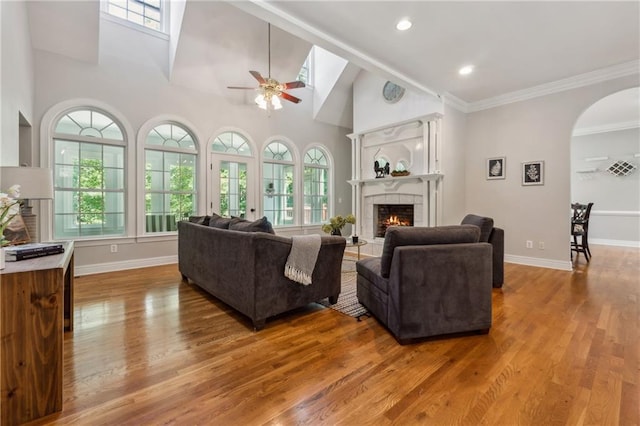 living room featuring hardwood / wood-style flooring, a tiled fireplace, ornamental molding, and ceiling fan