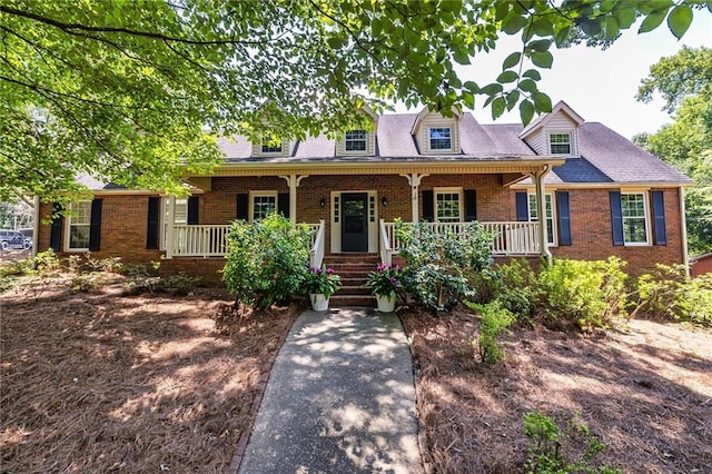 cape cod home featuring a shingled roof, a porch, and brick siding