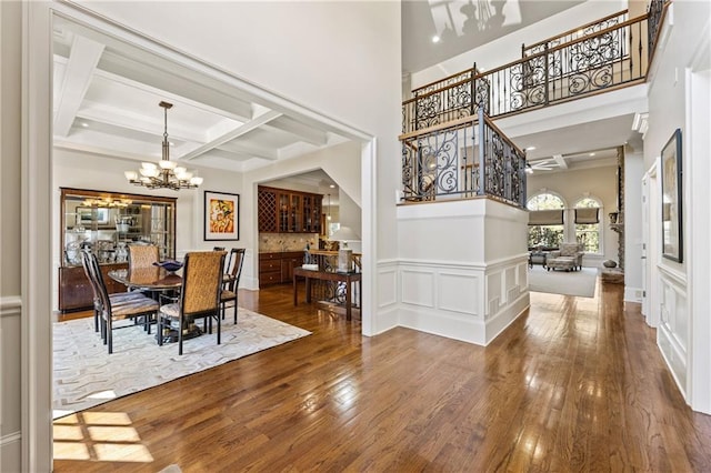 dining room featuring a towering ceiling, beam ceiling, coffered ceiling, hardwood / wood-style floors, and a chandelier