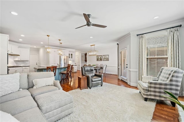 living room featuring ceiling fan with notable chandelier, recessed lighting, dark wood-style floors, and ornamental molding