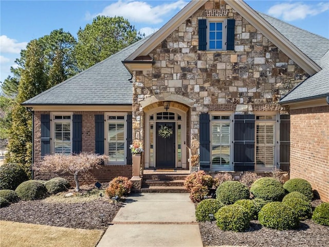 view of front of property featuring stone siding, brick siding, and a shingled roof