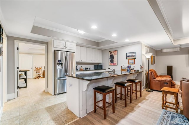 kitchen with white cabinetry, a tray ceiling, stainless steel fridge, and a kitchen bar