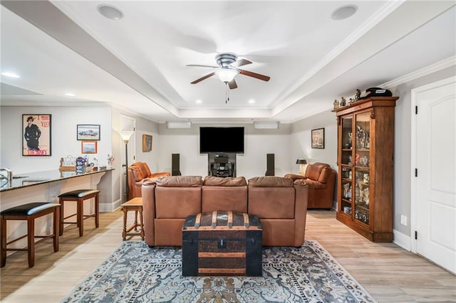 living area featuring a raised ceiling, ornamental molding, a ceiling fan, light wood finished floors, and baseboards