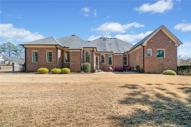 view of front of house with brick siding, a patio area, fence, and a front lawn