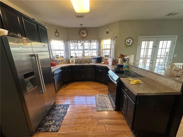 kitchen with sink, appliances with stainless steel finishes, light stone counters, light hardwood / wood-style floors, and kitchen peninsula