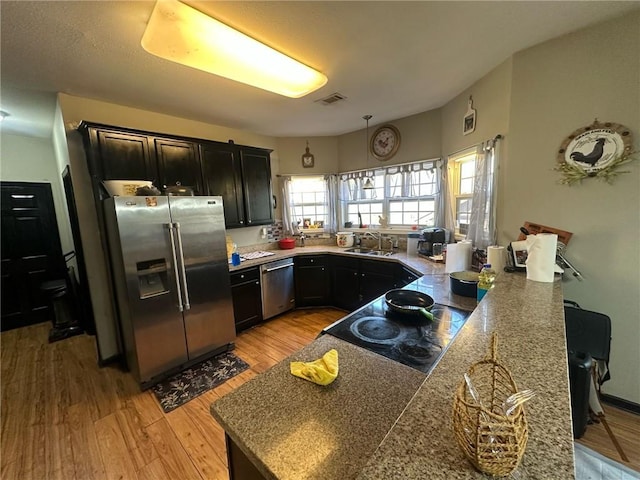 kitchen with sink, light wood-type flooring, appliances with stainless steel finishes, kitchen peninsula, and light stone countertops