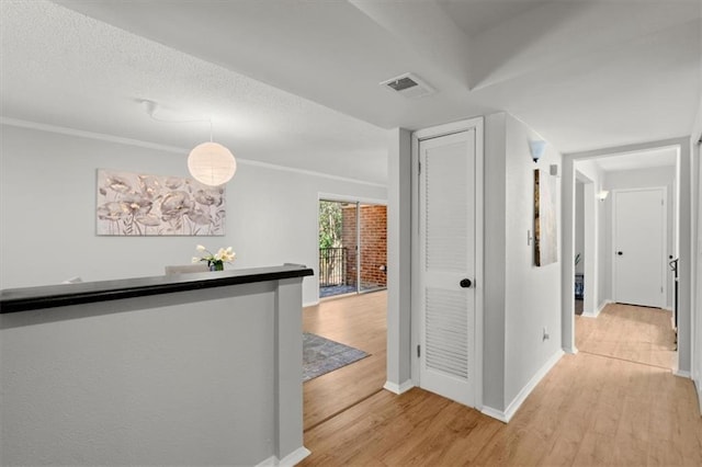hallway featuring crown molding, light hardwood / wood-style flooring, and a textured ceiling
