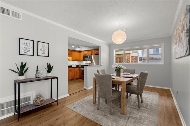 dining room with crown molding, light hardwood / wood-style flooring, and a textured ceiling