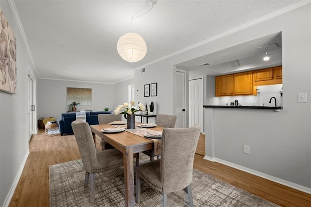 dining area featuring ornamental molding, a textured ceiling, and light wood-type flooring