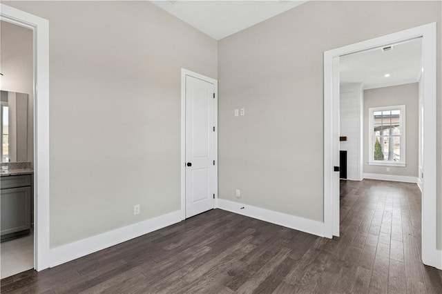 unfurnished bedroom with a large fireplace, ensuite bath, baseboards, and dark wood finished floors