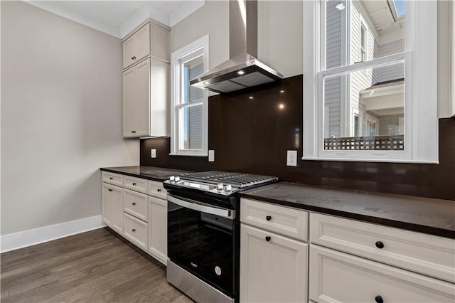 kitchen with dark countertops, dark wood-type flooring, ventilation hood, stainless steel gas range, and baseboards