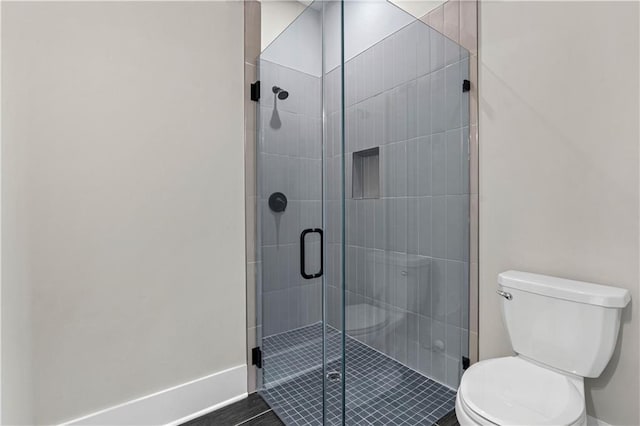 bathroom with a stall shower, toilet, and baseboards