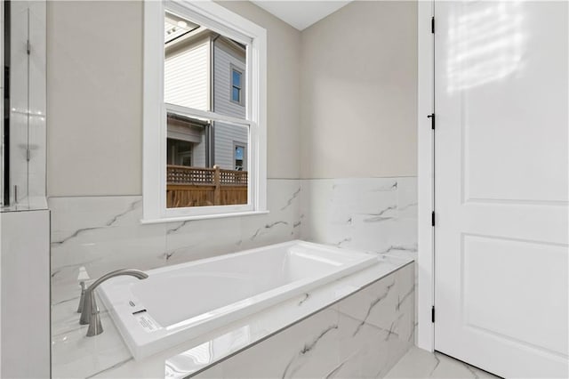 bathroom with marble finish floor and a bath