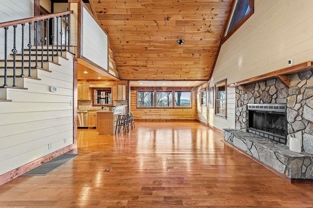 living room featuring a stone fireplace, wooden walls, high vaulted ceiling, and light hardwood / wood-style floors