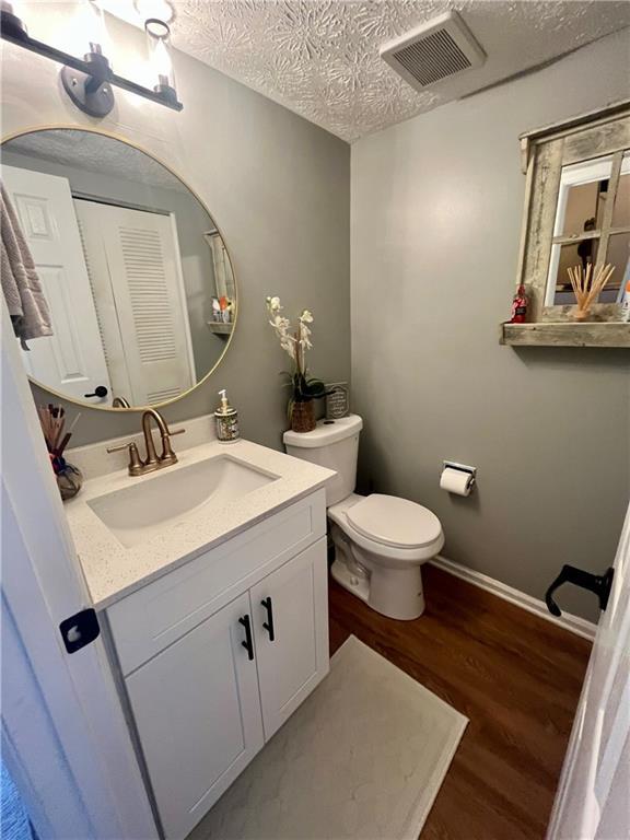 half bath with visible vents, toilet, vanity, wood finished floors, and a textured ceiling