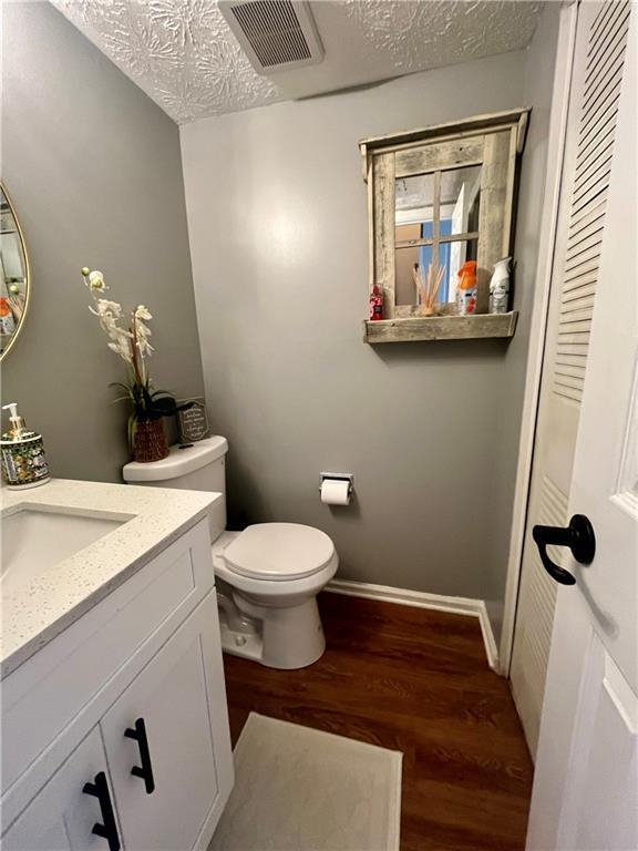 bathroom with visible vents, toilet, wood finished floors, and a textured ceiling