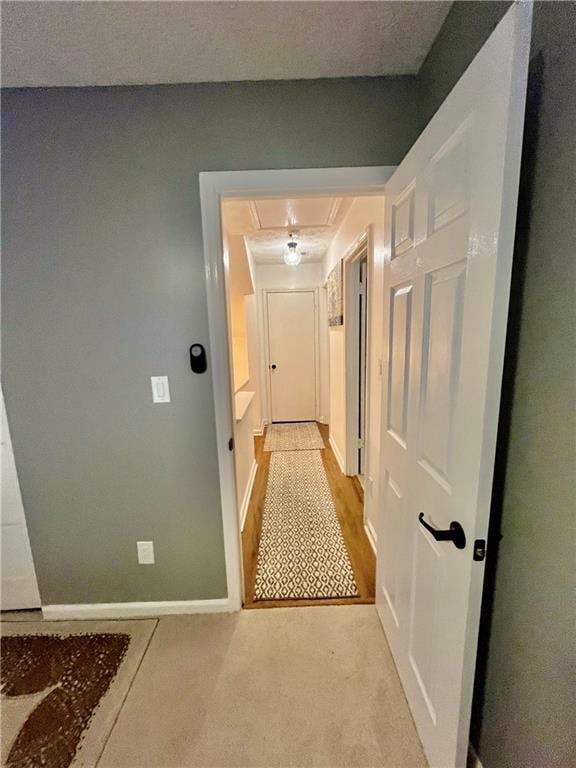 hallway with attic access, baseboards, and light carpet