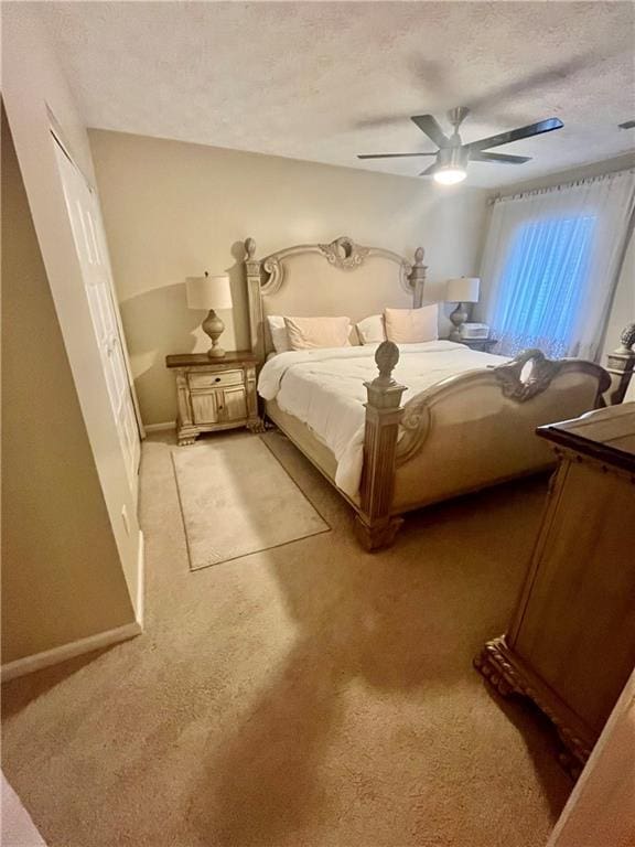 bedroom featuring baseboards, light carpet, a textured ceiling, and ceiling fan