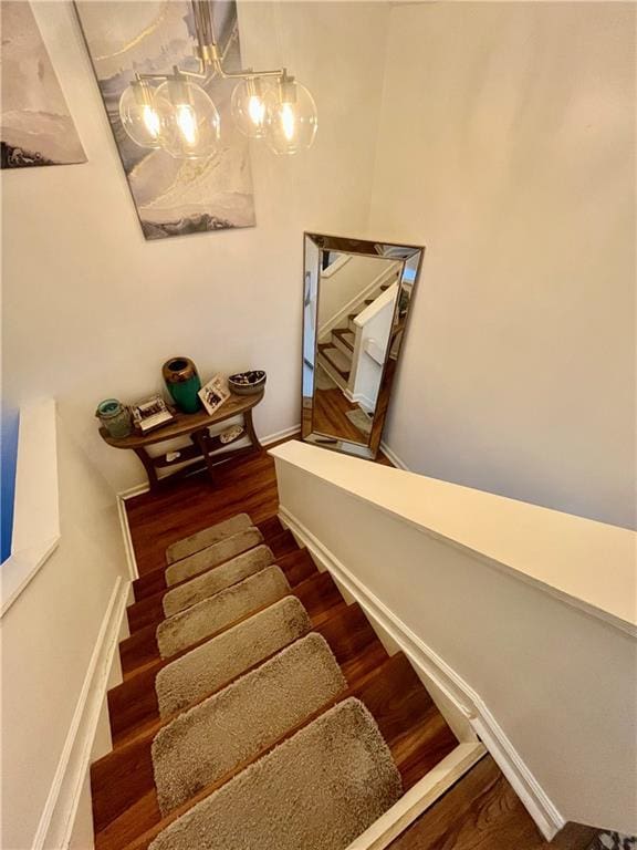 stairway featuring a notable chandelier, wood finished floors, and baseboards