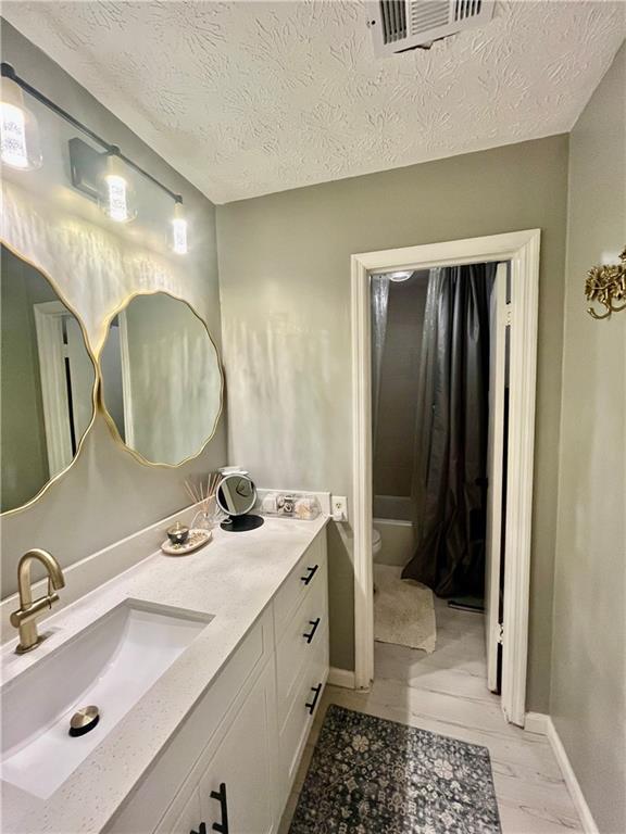 bathroom with vanity, baseboards, visible vents, a textured ceiling, and toilet