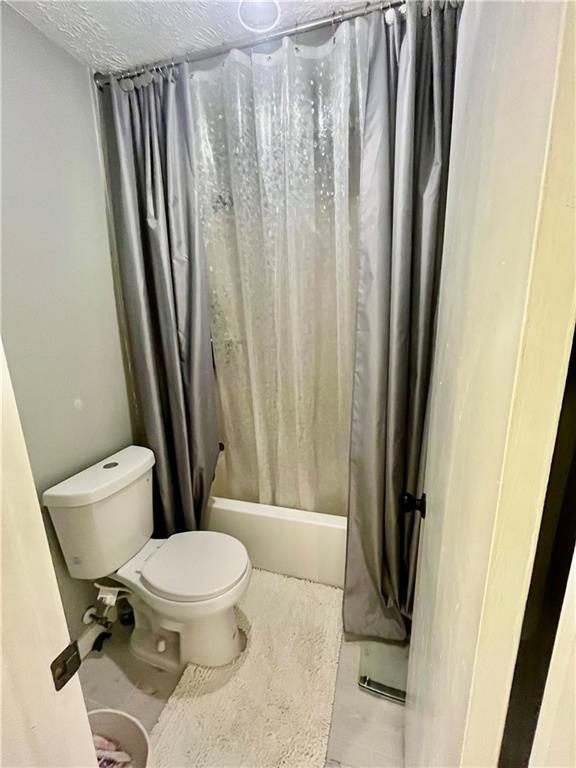 full bath featuring toilet, shower / bath combo, and a textured ceiling