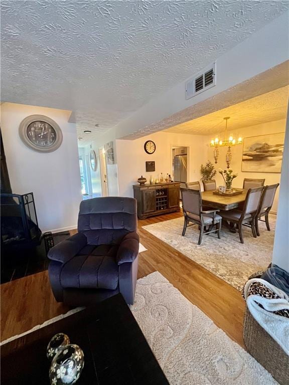 living area featuring a chandelier, visible vents, a textured ceiling, and wood finished floors