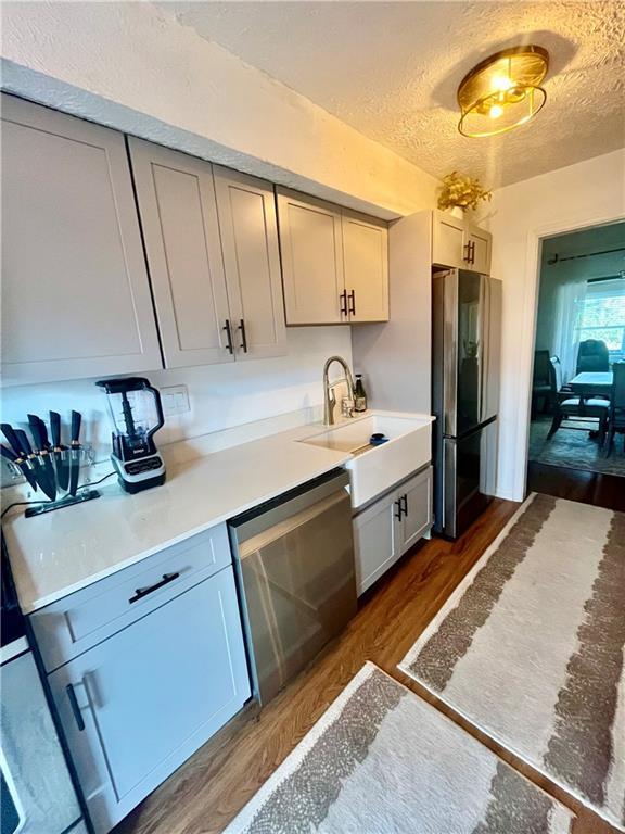 kitchen with dark wood-style floors, a sink, light countertops, appliances with stainless steel finishes, and a textured ceiling