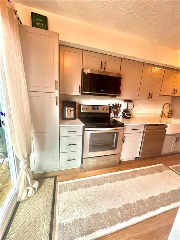 kitchen with light wood-style flooring, a sink, a textured ceiling, appliances with stainless steel finishes, and light countertops